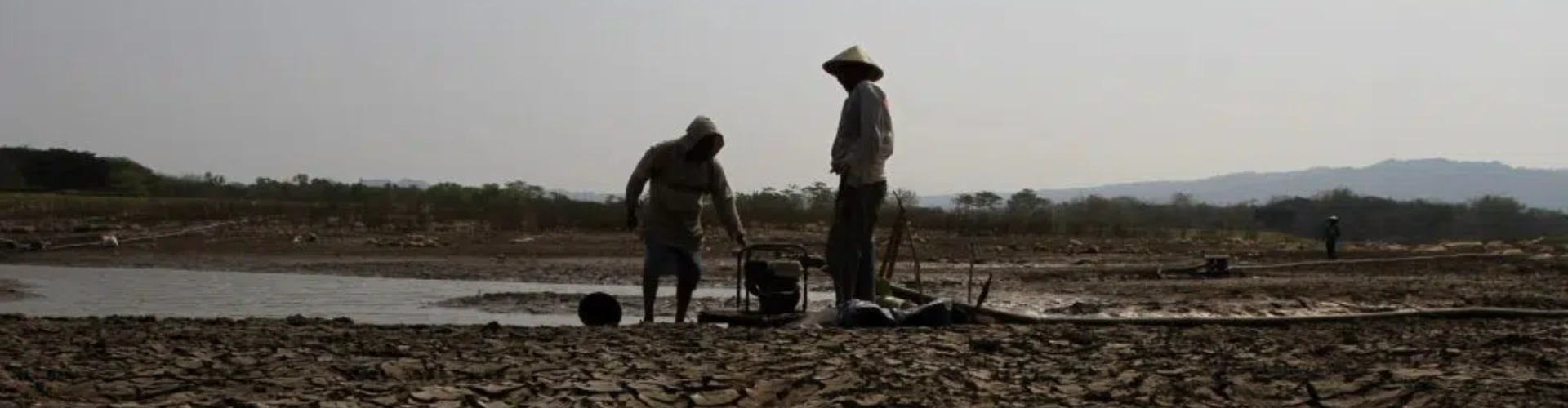 2 farmers with a petrol powered pump between them moving water into their drought affected fields during the heatwave in Asia