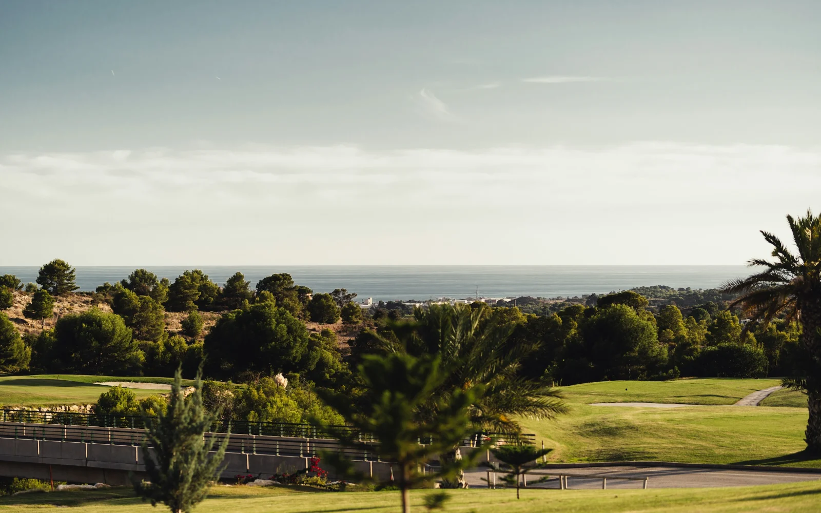A golf course with fairway, bunker and trees above a distant coastline. Industry context, not a course assessed in the register.